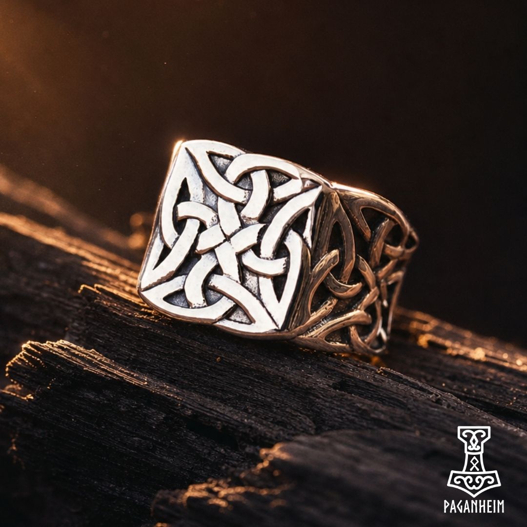 A silver-toned Viking-style ring with an intricate knotwork design on a square face, resting on a dark textured wooden surface.