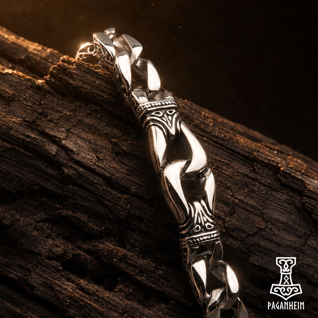 A polished silver-toned metal Viking-style chain bracelet with ornate engraved details, resting on a dark textured piece of wood.