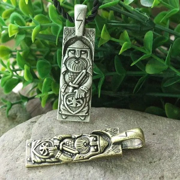 Decorative pendant with warrior design on a stone surface with green leaves in the background