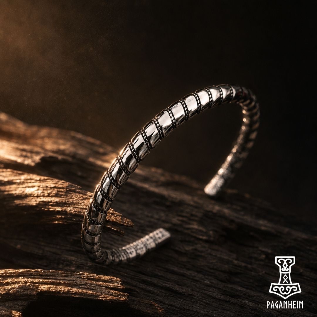 A silver-toned open cuff bracelet with a textured, segmented pattern, resting on a dark, rustic wooden surface under dramatic warm lighting.