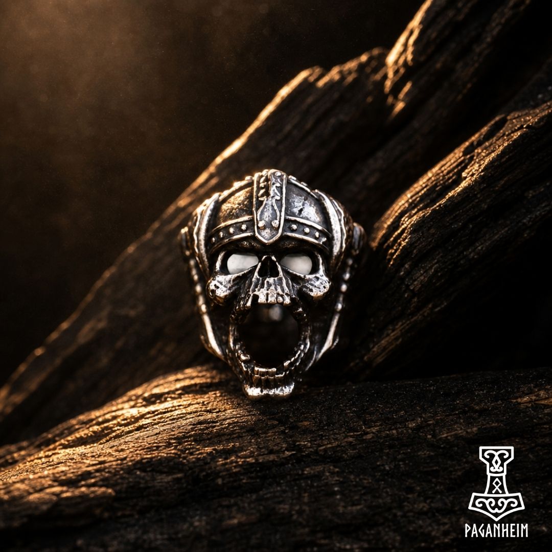 A Viking-style skull ring in polished silver-toned metal, resting on a textured piece of dark wood.