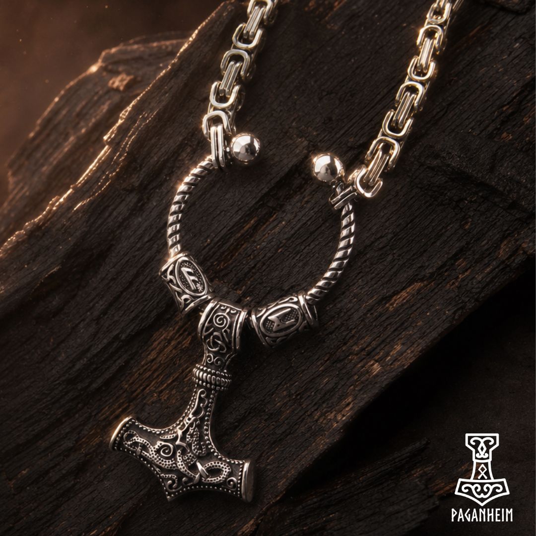 An ornate silver-toned Viking-style hammer pendant necklace with detailed engravings, displayed on a dark textured wooden surface.