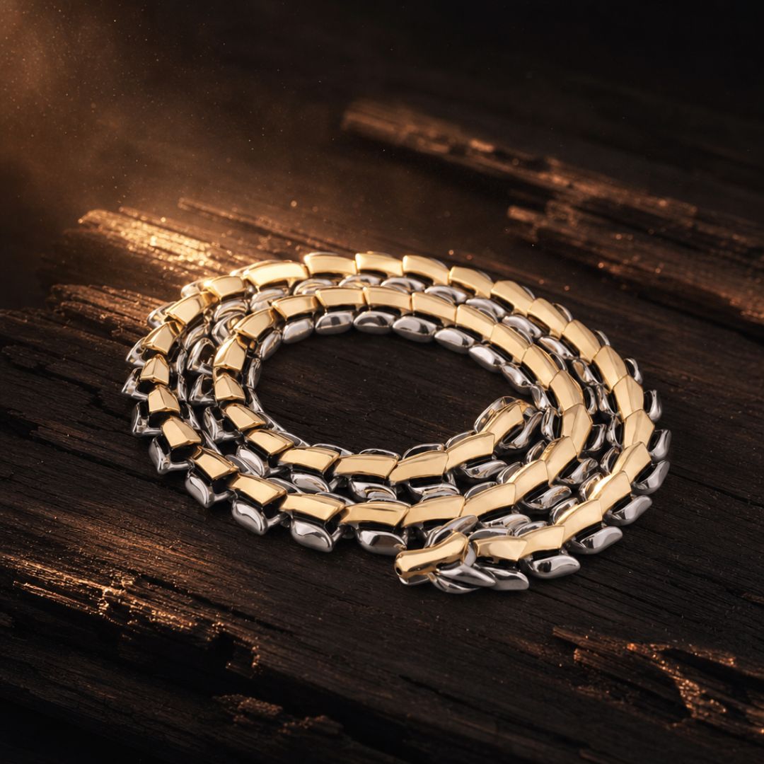 A coiled two-tone chain necklace with gold and silver links, displayed on a dark, rustic wooden surface with dramatic golden lighting.