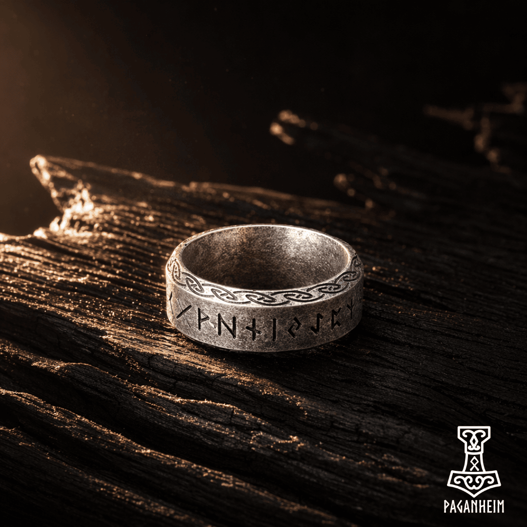 Silver ring with engraved Elder Futhark runes on a dark wooden surface.