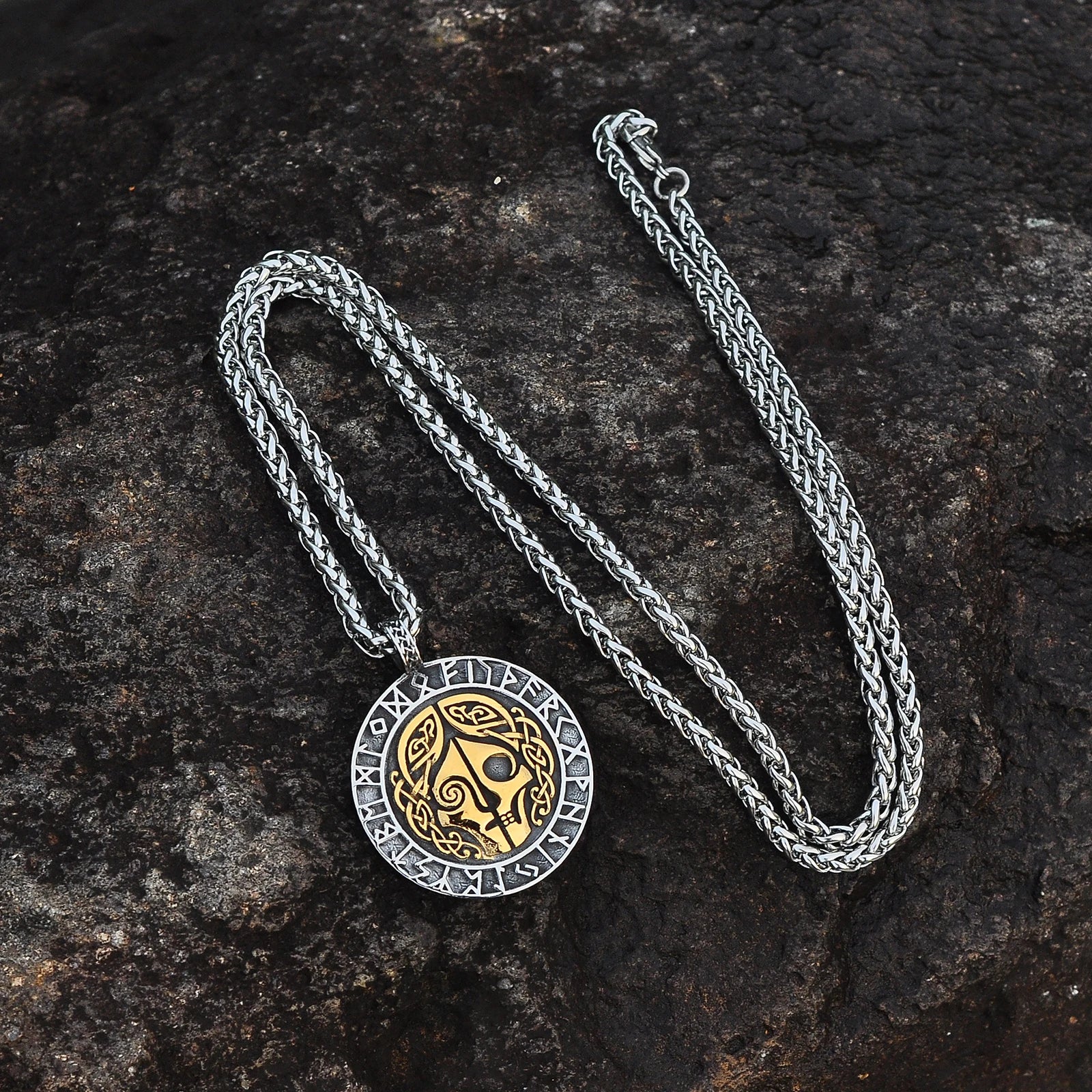 Front of the pendant depicts Hel with a gold and silver-coloured split face; the back features the Vegvísir symbol encircled by runes.