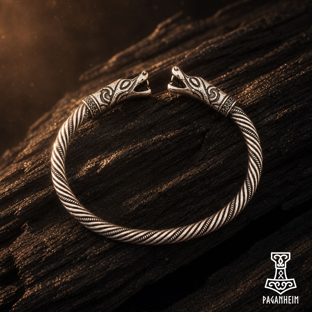 A silver-toned Norse-style cuff bracelet with carved animal head closures and a twisted rope texture, displayed on a dark wooden surface. 