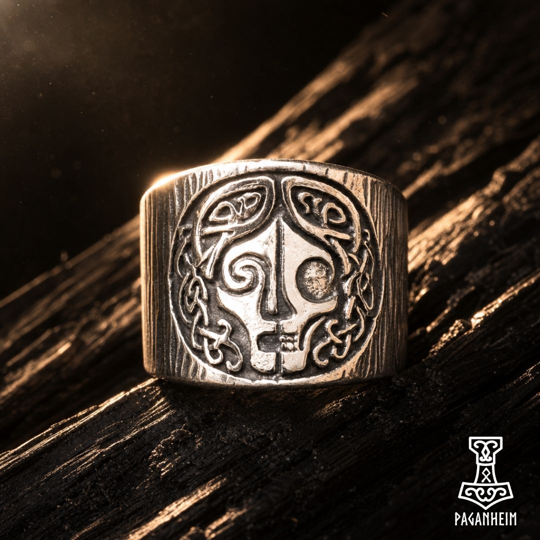 A silver-toned Viking-style ring with an engraved skull and knot design, resting on a dark textured wooden surface with dramatic warm lighting.