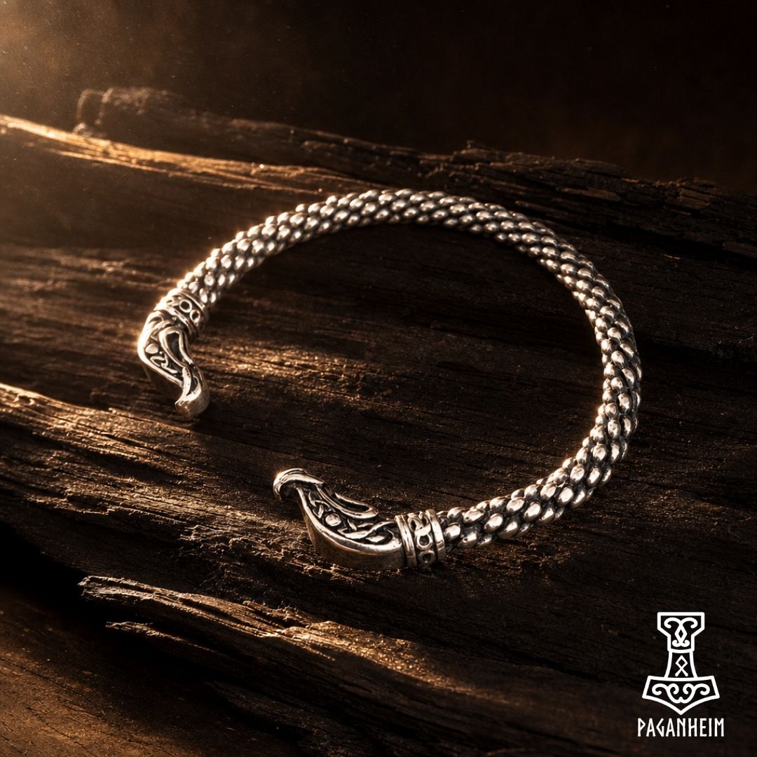 A silver-toned Viking-style cuff bracelet with ornate dragon-head closures, displayed on a dark textured wooden surface.