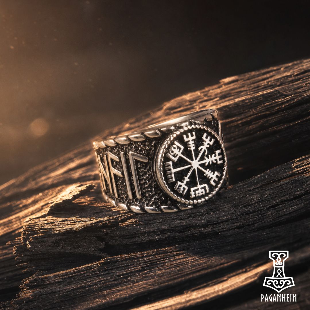 A silver-toned Viking-style ring with a compass and runic design, resting on a textured piece of wood with dramatic warm lighting.