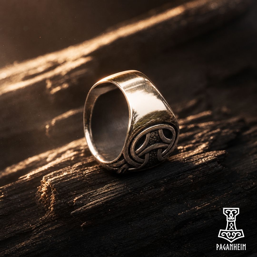 Serpent‑encircled Vegvísir ring resting on dark wood surface under warm light