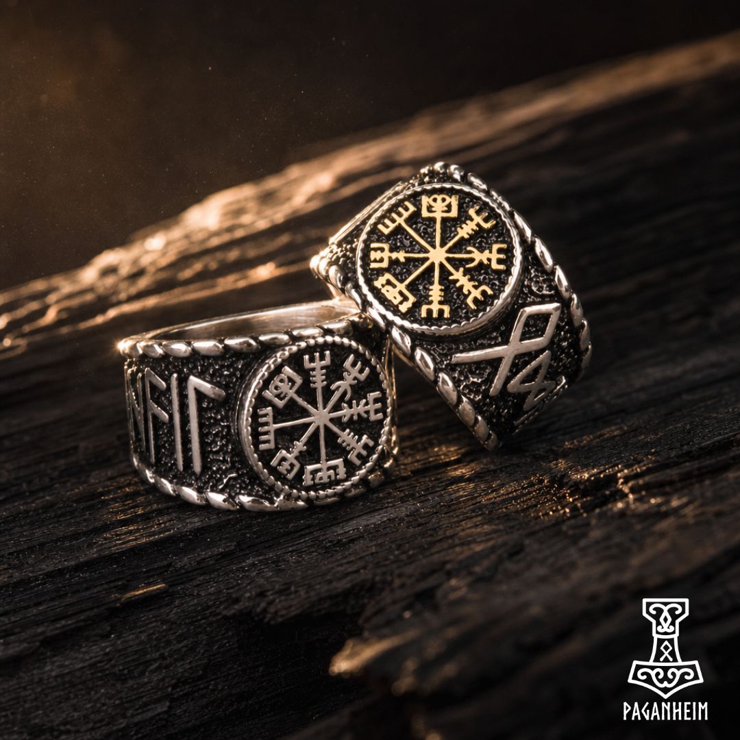 Two Norse-style Viking rings with engraved runes and a Vegvisir compass design, displayed on a dark wooden surface. One ring is silver-toned and the other is gold-toned, both featuring textured rope bands.