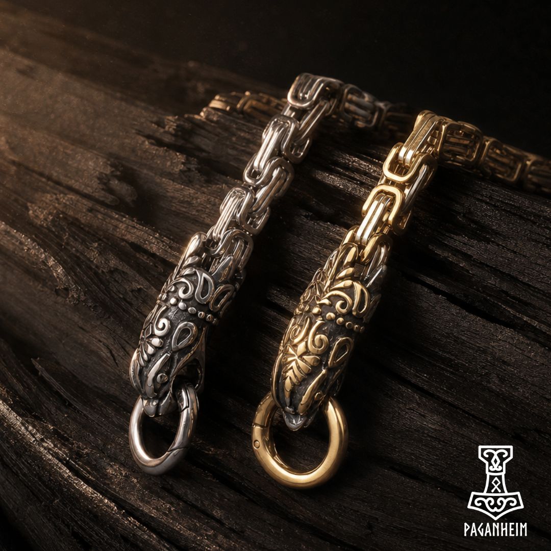 Two ornate Viking-style chain links with detailed relief carvings, one in silver-toned metal and one in gold-toned metal, displayed on a dark textured wooden surface.