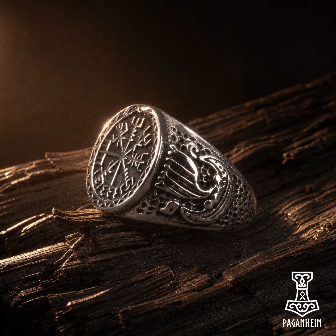 A silver-toned Viking-style ring with engraved runes and a longship motif, resting on dark textured wood with dramatic warm lighting.