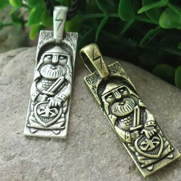 Two Viking-themed pendants on a stone surface with greenery in the background