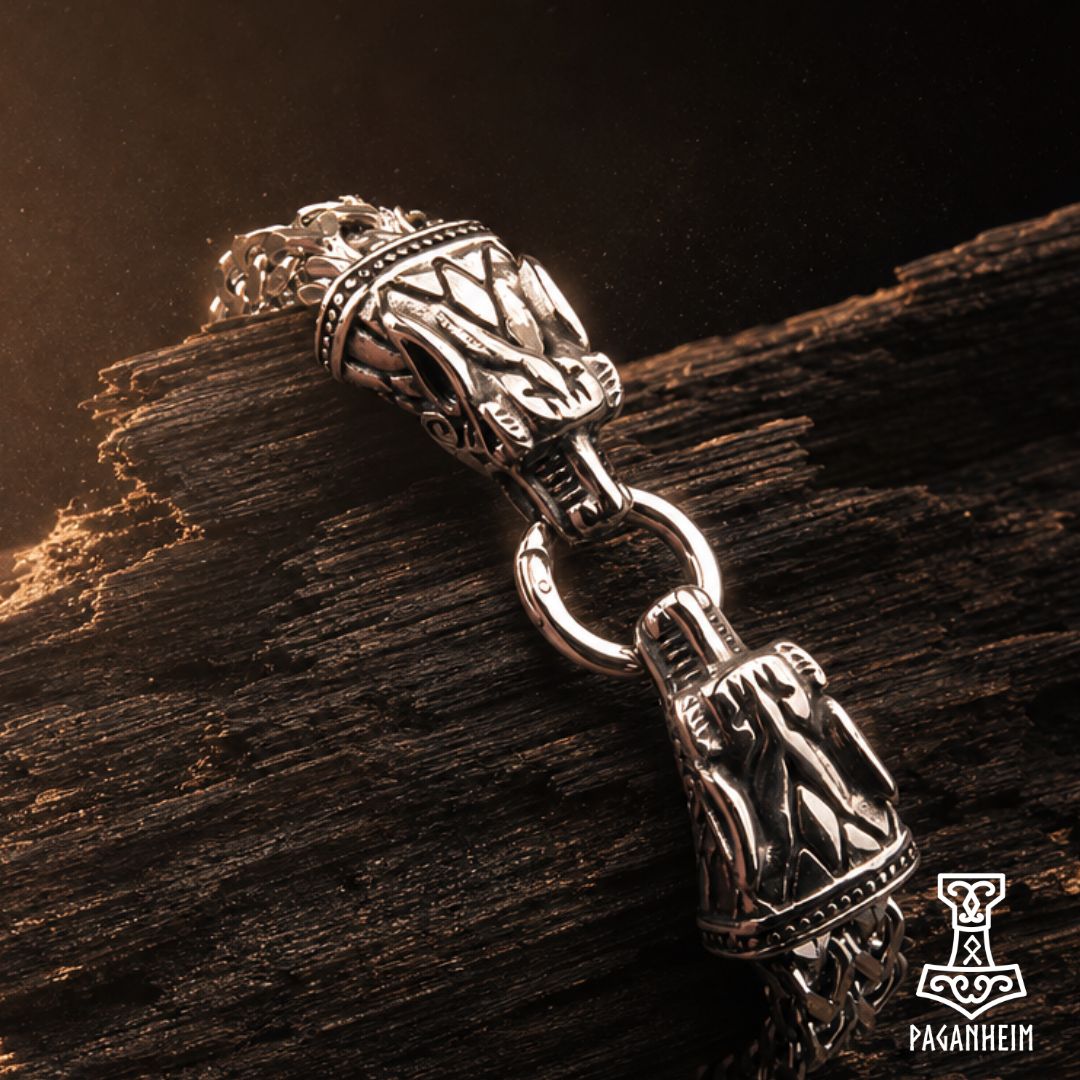 A close-up of a silver-toned Viking-style pendant or charm with carved details and a ring connector, resting on a textured piece of dark wood against a dark background.
