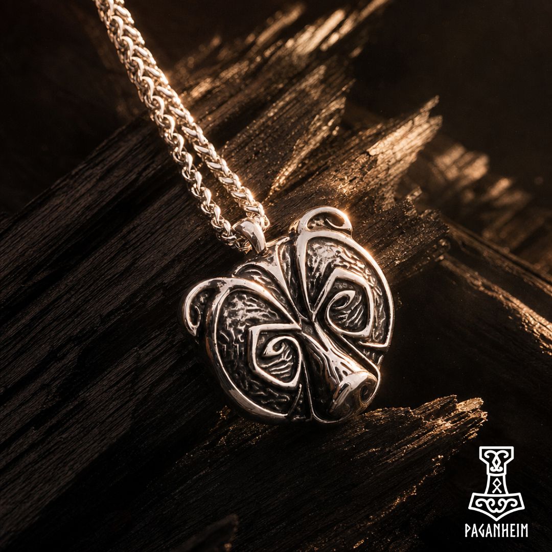A silver-toned Norse-style pendant necklace with an intricate knotwork design, hanging from a braided chain against a dark textured wooden background. The brand logo 'Paganheim' is visible in the bottom right corner.