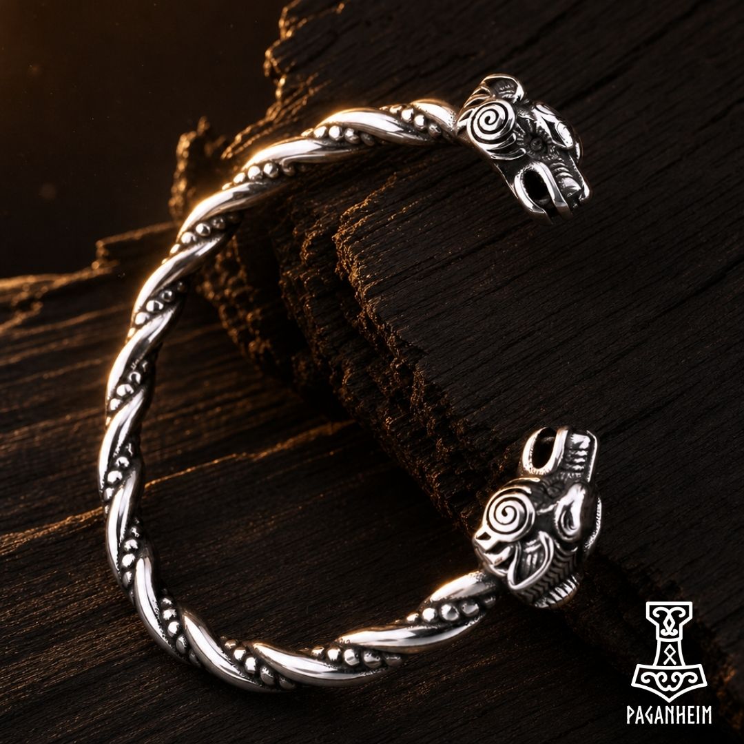 A silver-toned twisted metal cuff bracelet with animal head closures, displayed on a dark textured wooden surface.