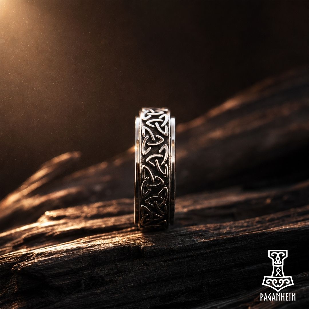 A silver-toned Celtic knot ring stands upright on a dark textured wooden surface, illuminated by dramatic warm light from the upper left.