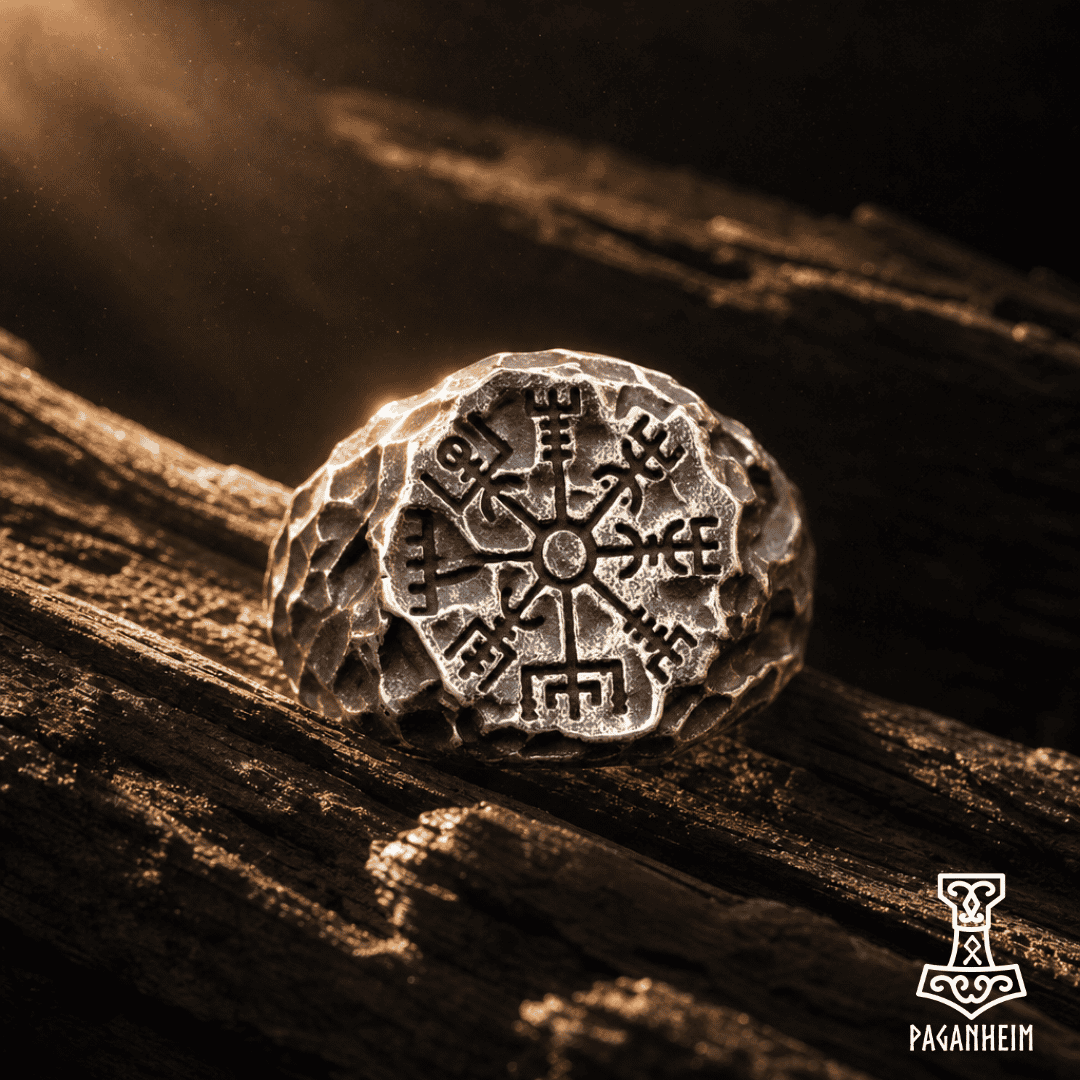 A textured silver-toned ring featuring an engraved Norse-style compass or Vegvisir symbol, resting on a dark, rustic wooden surface with dramatic warm lighting.