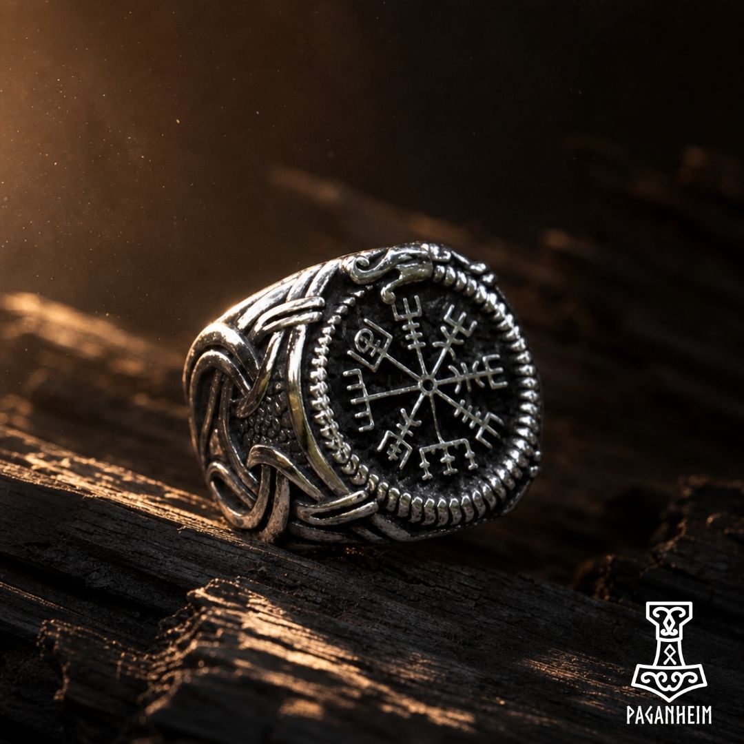 A stainless steel ring featuring a Norse Vegvísir symbol on the top, with decorative patterns around it, placed on a textured surface.