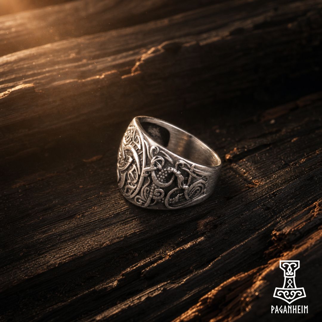 An ornate silver Viking-style ring with intricate knotwork and a hammer motif, resting on a dark, textured wooden surface. The brand logo 'Paganheim' is visible in the bottom right corner.