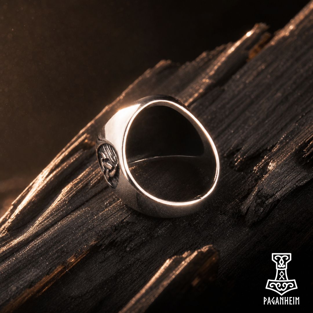 A silver-toned Viking-style ring with a carved skull detail, resting on dark textured wood. 